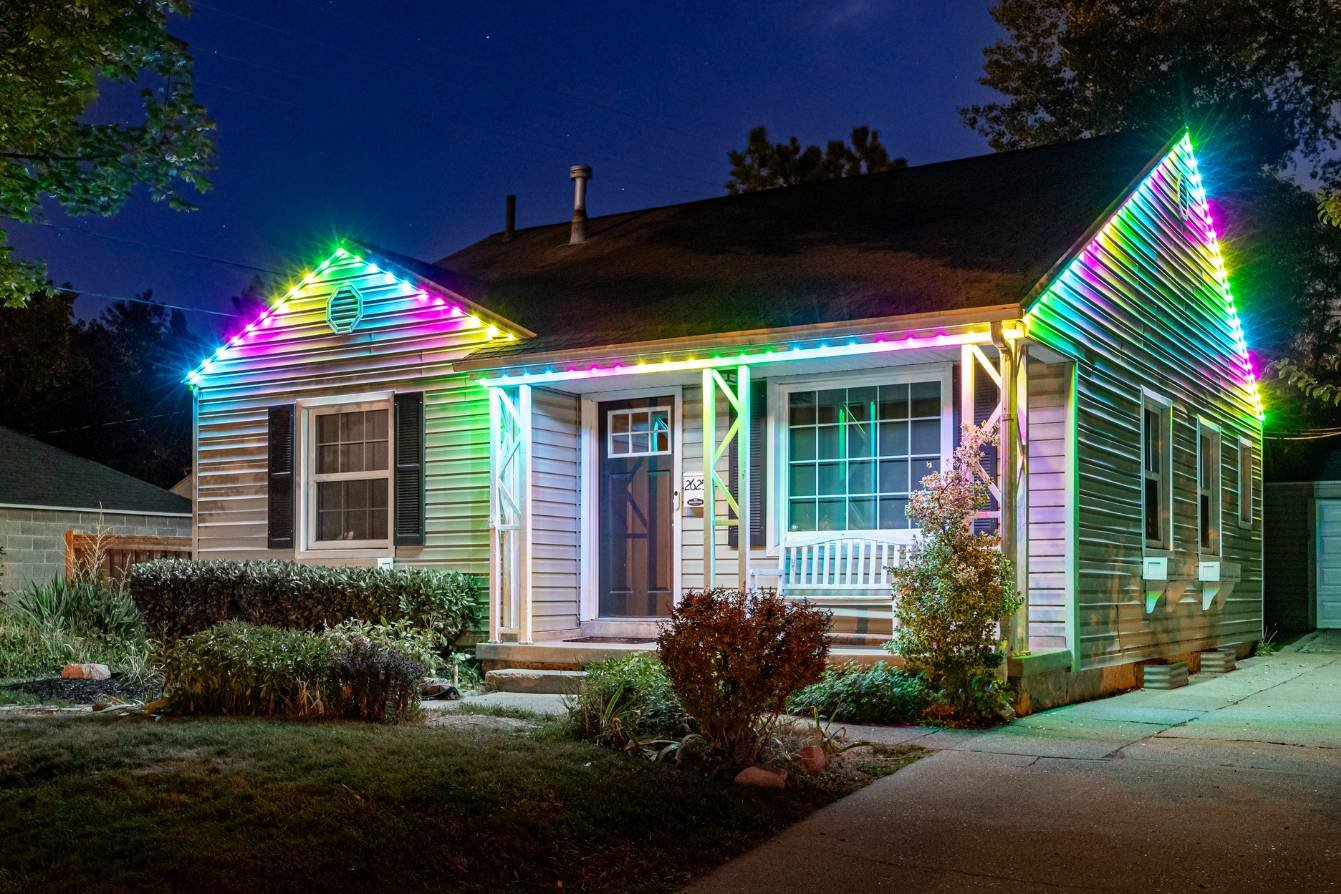 A white small home with pink, yellow, green, and blue Trimlight lighting.