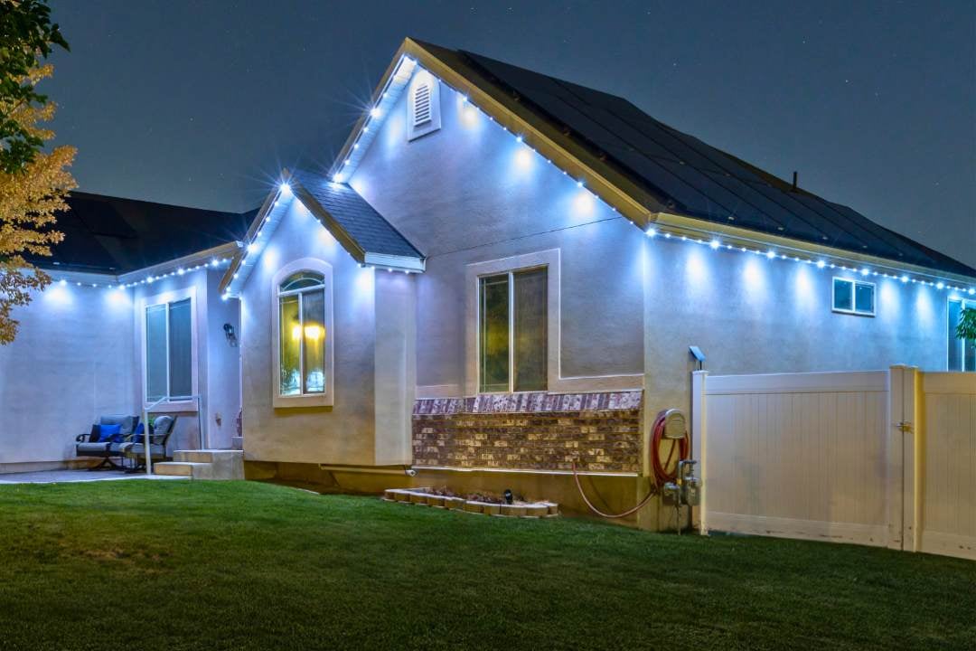 Home with a tree and white fence. This home has Trimlight 3L featuring a security pattern.