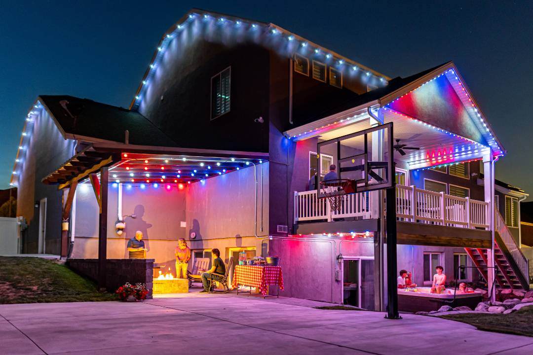 Outdoor holiday lights showing on a massive hime with globe lights and people standing under them.