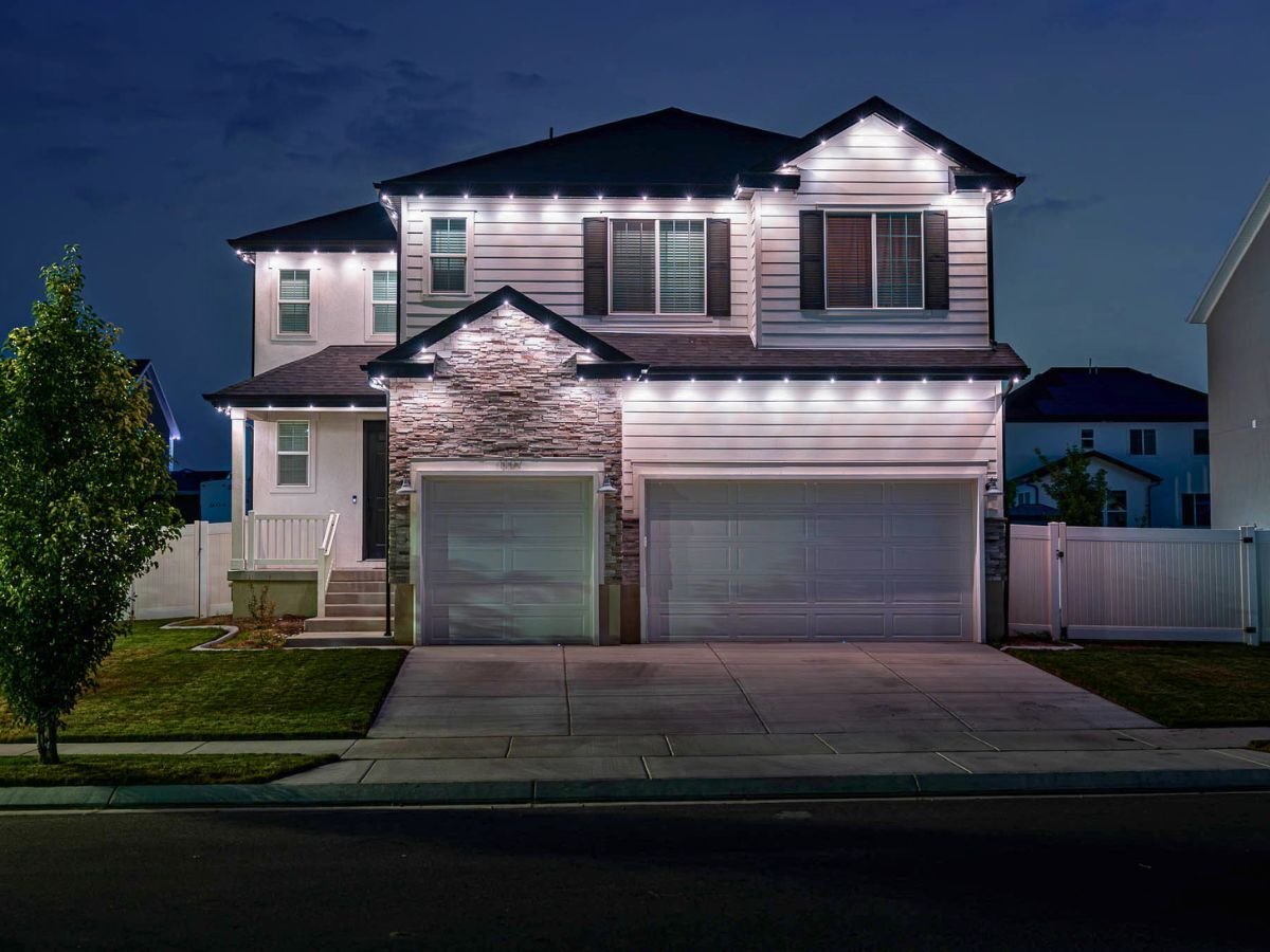 A home with an accent lit lighting pattern with a tree in front.