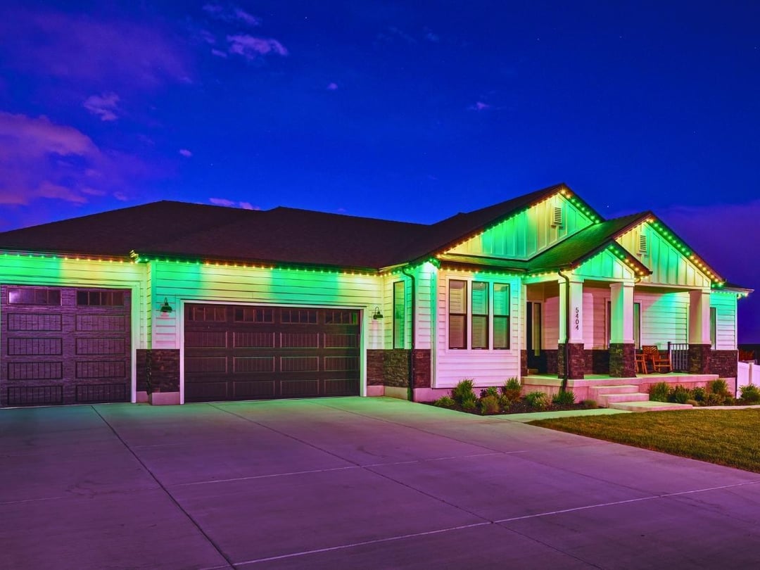 A home that has 3 peaks and a longer body. It has a large driveway with a green and yellow Trimlight lighting pattern.