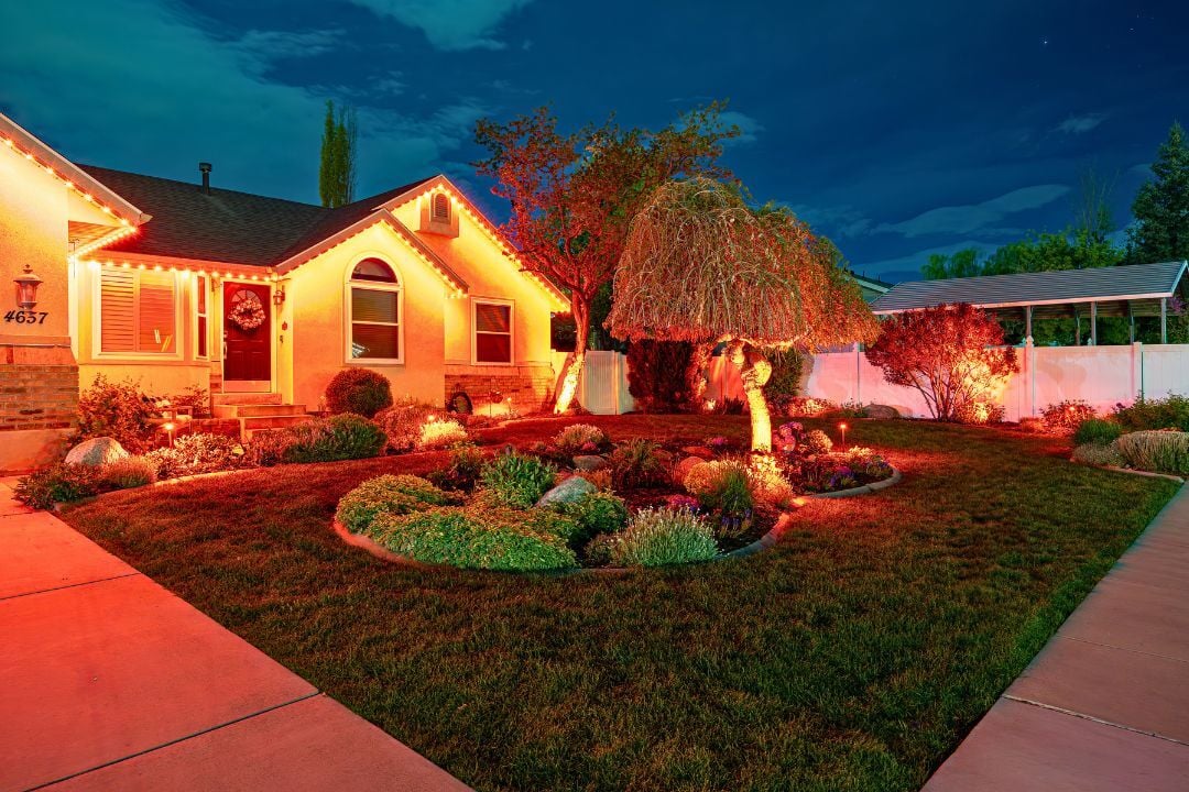 A picture of a home with orange lighting with nice landscape lighting in front of the home.