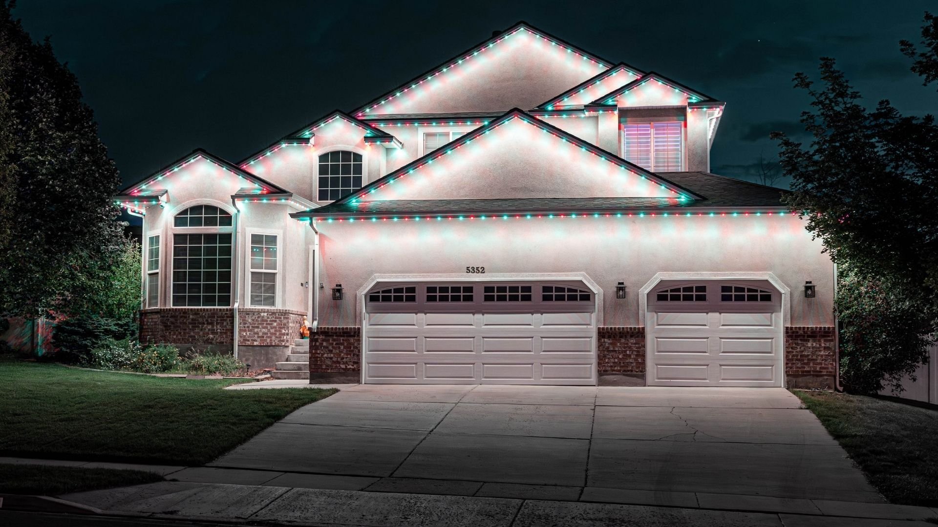 A home with a simple Christmas Trimlight pattern that has a white glow on the home and a big driveway.