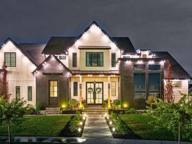 A picture of a home with a lit up pathway leading to their house. it has a darker facia in some places which shows the light splash in different places.