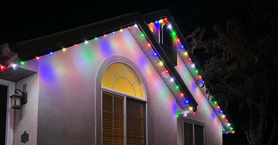 White stucco home with Charlie Brown Christmas color lighting around soffit of home