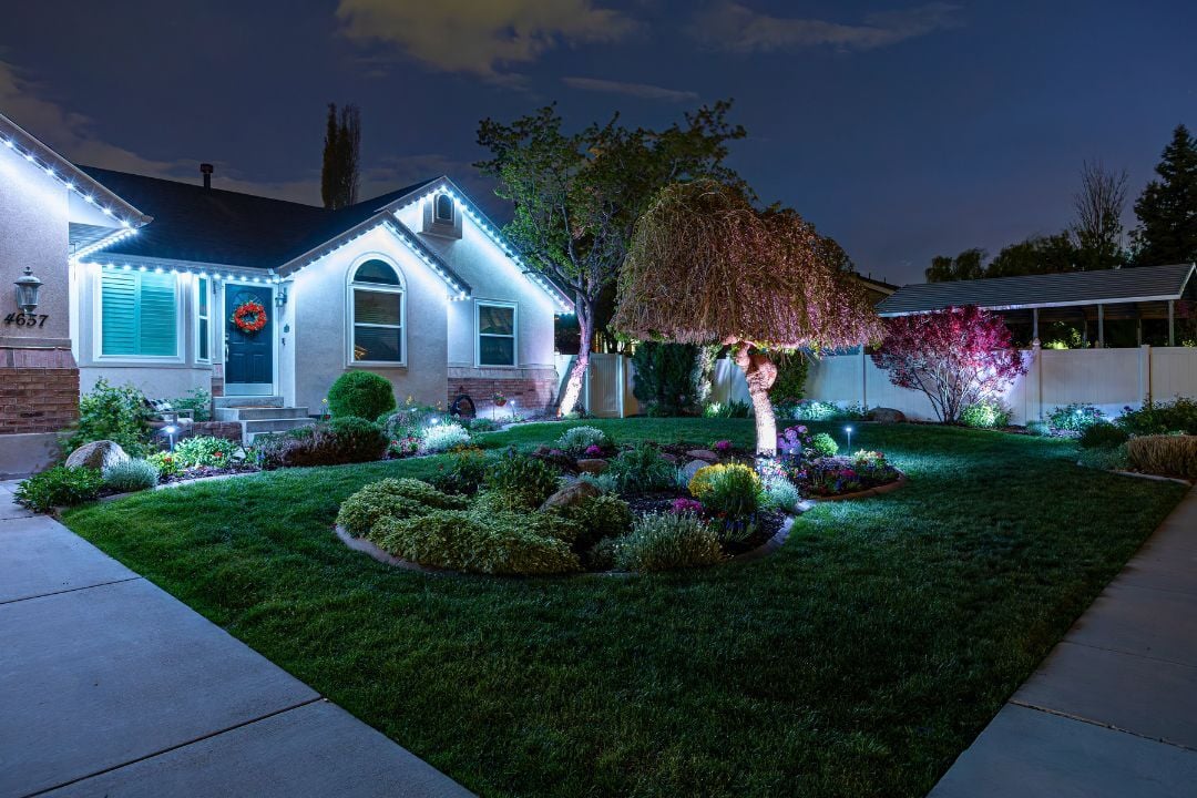 a image with a cool white glow with landscape lighting shining against the trees and Trimlight lighting on the house.