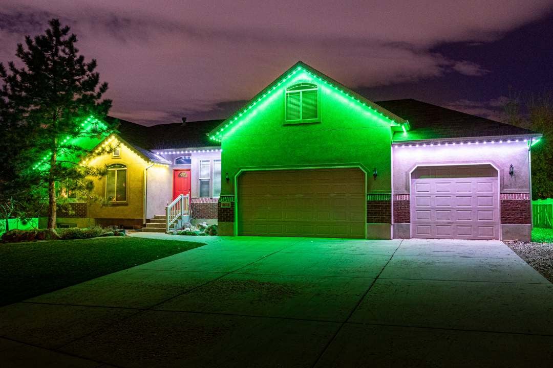 Green, yellow, and white trim lighting on stucco home at night.