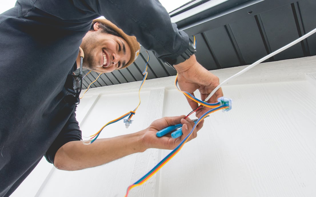 a picture of a Trimlight installer cutting some wire with some black soffits above him