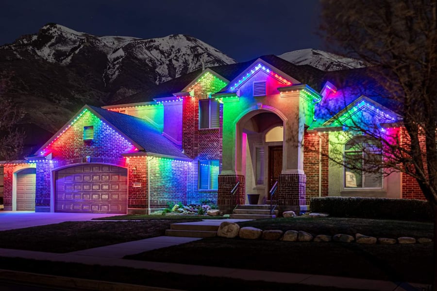 A large home with a mountain in the background  and on the home it features a rainbow Trimlight pattern.