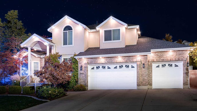 Brick and white stucco home with white garages at night with trim lighting on front.