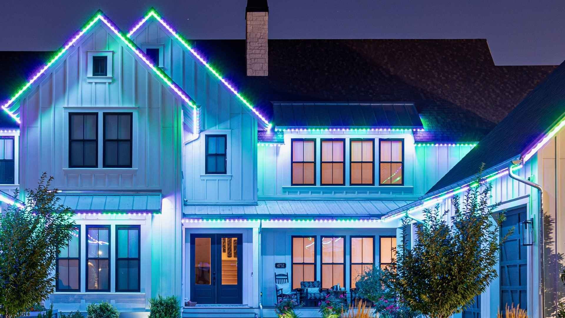 A beautiful home with 2 peaks that has a purple and green Trimlight lighting pattern and has 2 trees in front.