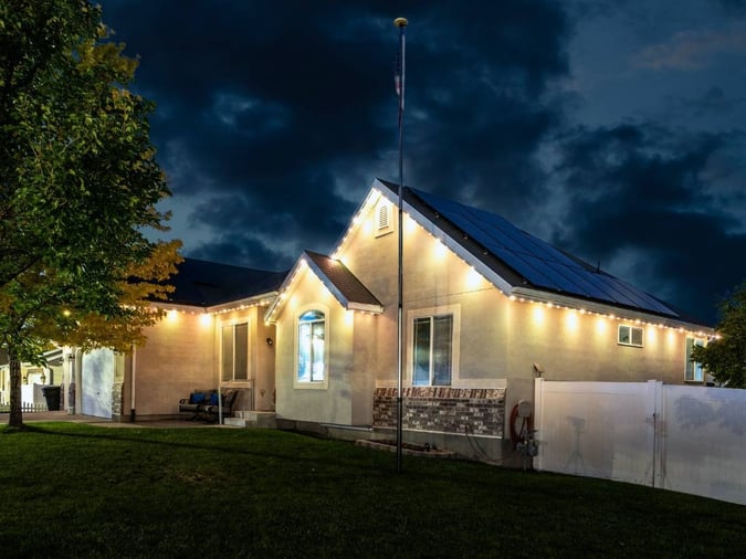 A picture of a home with a warm white lighting on the home. It has a pole in the front and has a tree on the left side of the image.