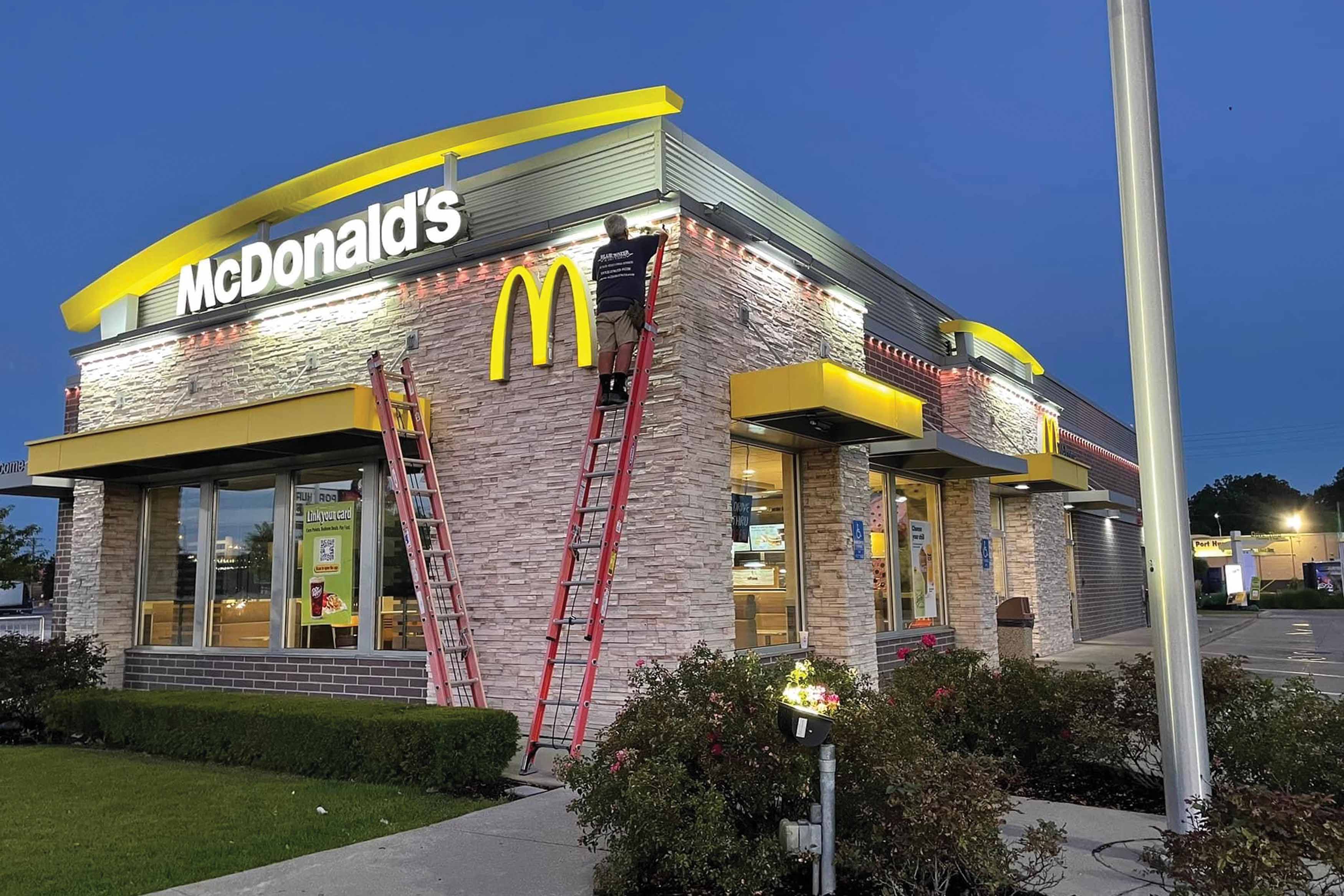 a McDonalds restaurant with a person on a ladder with bright Trimlight LEDs
